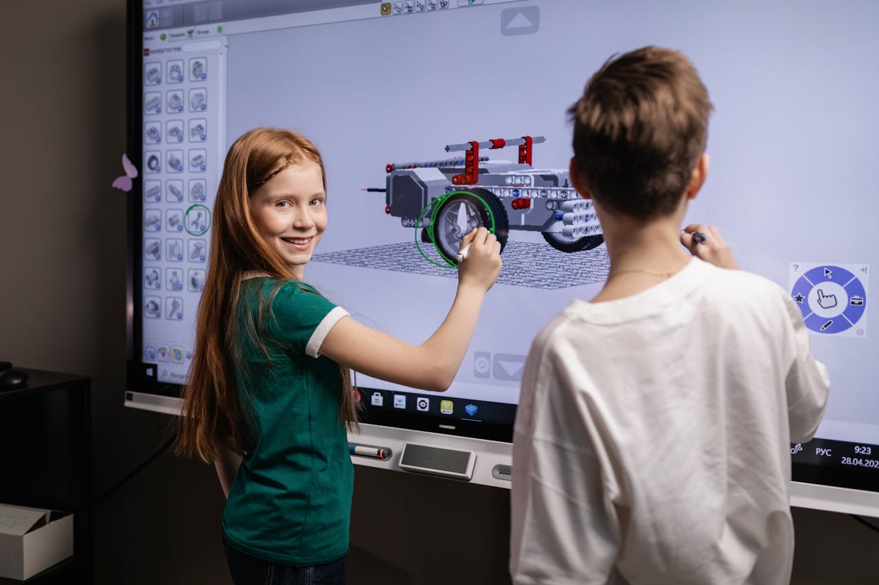 about-04 Two children interacting with a digital screen in a classroom setting, learning through technology.