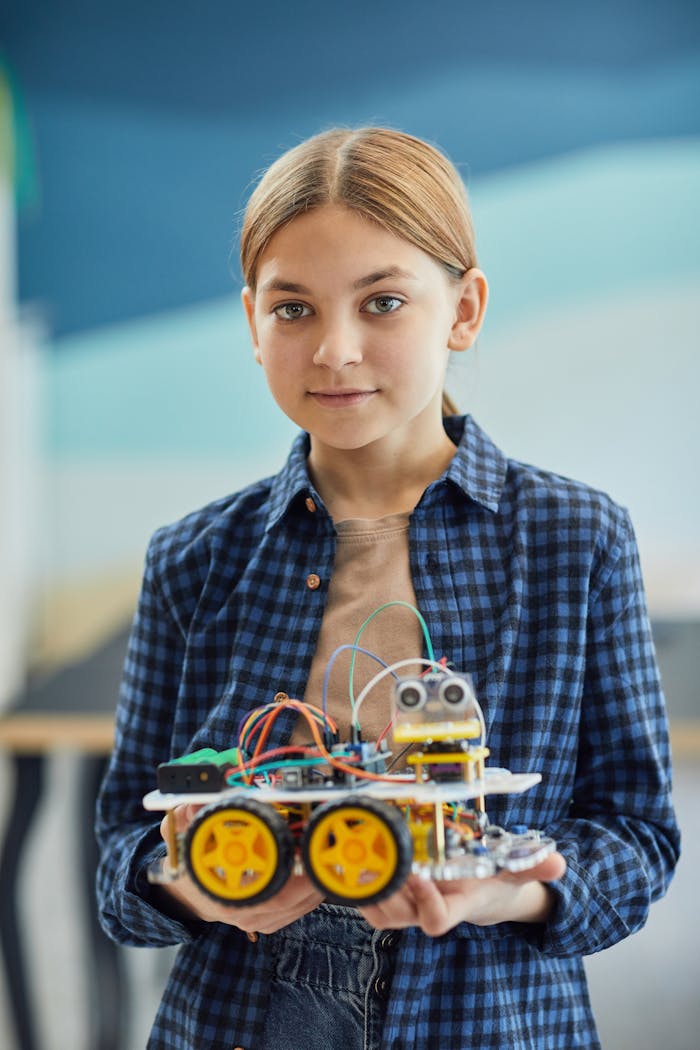 menu-08 A young girl in a checkered shirt holds a DIY robotic project, showcasing technology and creativity.