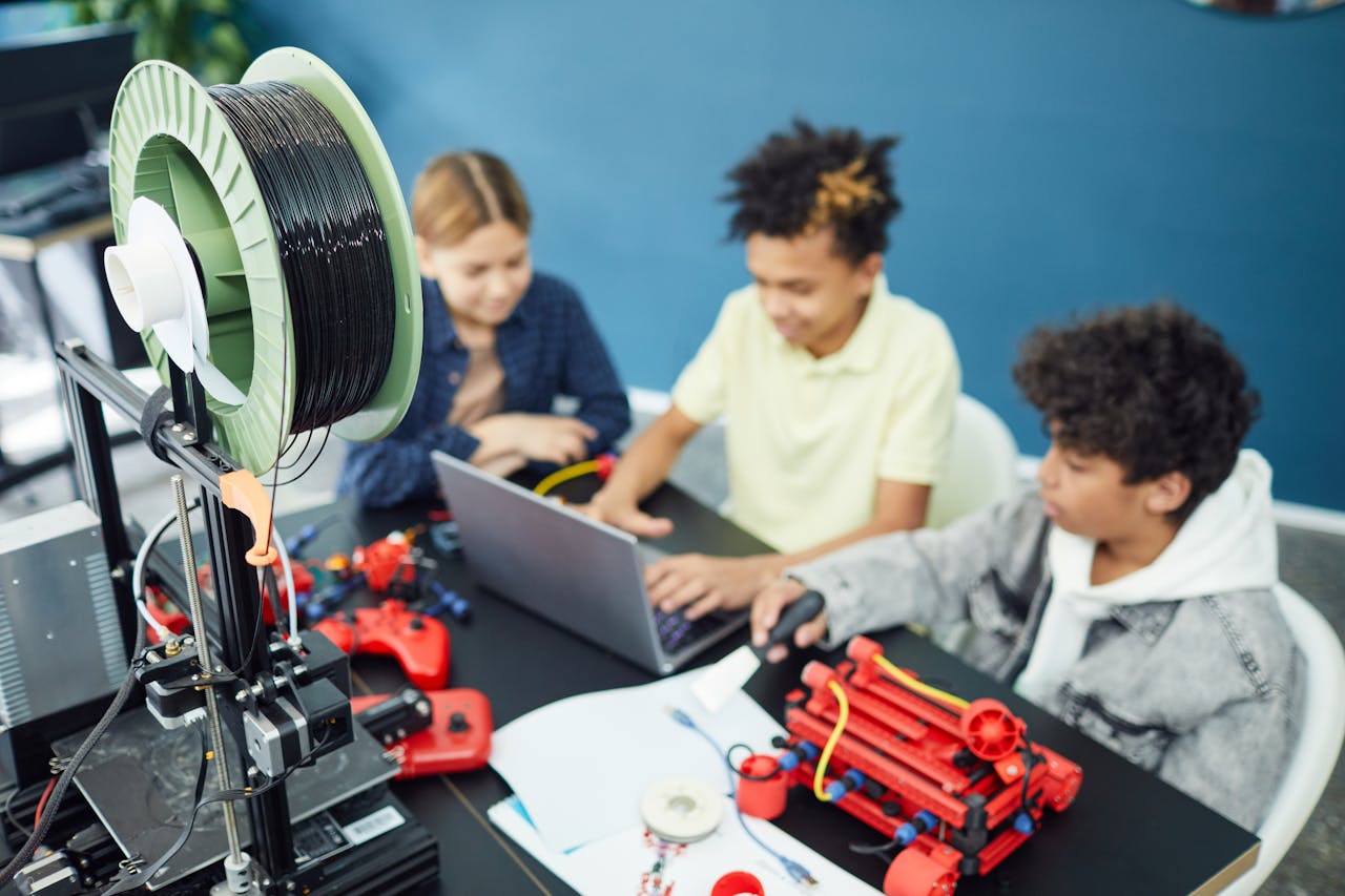 menu-02 Children collaborating on a STEM project with a 3D printer and laptop in an educational setting.